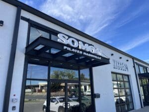Exterior of SOMOS Pilates Nashville, showing the entrance with a glass door and sign, under a blue sky.