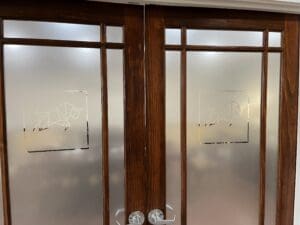 Double wooden doors with frosted glass panels, each featuring an etched geometric bull design at the center.