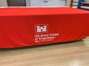 A red tablecloth with the US Army Corps of Engineers Nashville District logo and text displayed on a wooden floor.