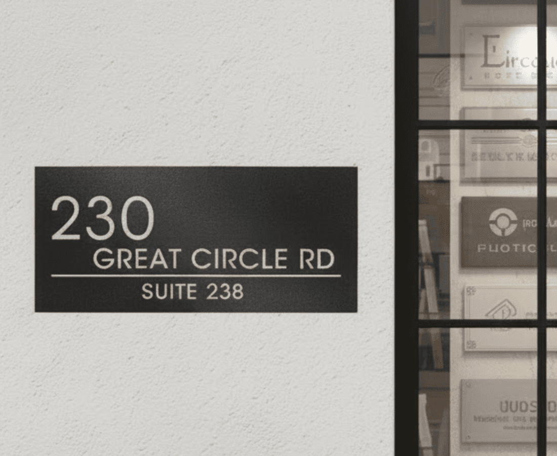Black and white sign on a wall reads "230 Great Circle Rd, Suite 238"; to the right is a glass window showing blurred signage inside.