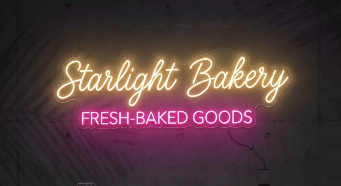 Neon sign with "Starlight Bakery" in yellow cursive and "FRESH-BAKED GOODS" in pink capital letters on a dark background.