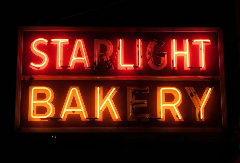Neon sign reading "Starlight Bakery" illuminated in red and yellow against a dark background.