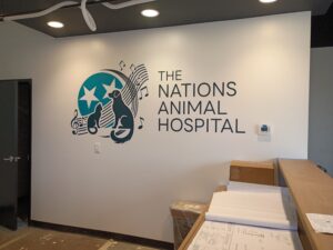 Wall with "The Nations Animal Hospital" sign, featuring animal silhouettes and musical notes, surrounded by construction materials and blueprints in an unfinished room.