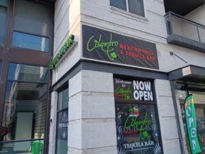 Storefront of "Cilantro Mexican Grill & Tequila Bar" with signs indicating it is now open, located on the ground floor of a modern building.