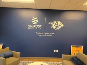 Blue wall with Vector Security and Nashville Predators logos, "Preferred Partner of the Nashville Predators" text, and framed hockey jerseys on the floor.