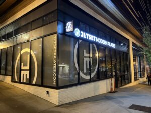Exterior view of a Jet Set Modern Pilates studio at night, with illuminated signage and large logo graphics on the windows.