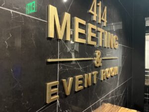 Gold lettering on a black marble wall reads "414 Meeting & Event Room"; a green "EXIT" sign is visible at the top left.