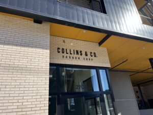 The entrance of Collins & Co. Barber Shop, with black signage on a light brick wall and glass doors beneath.