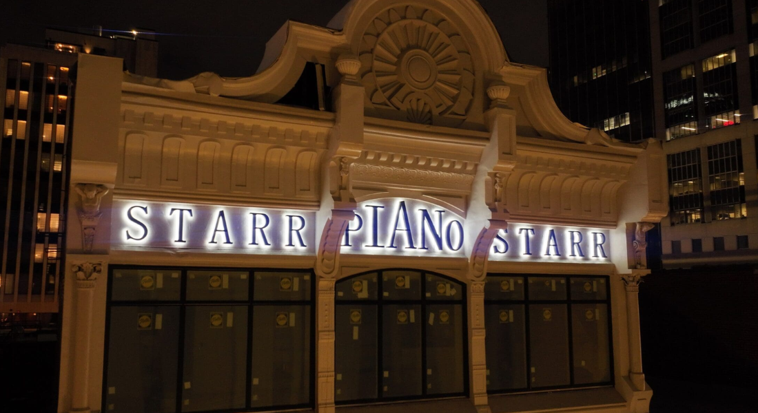 A white building at night displays illuminated signage reading "STARR PIANO STARR" above its windows, with architectural details visible on the facade.