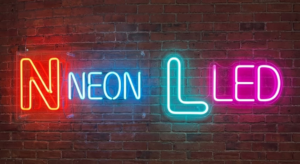 Neon sign on brick wall reads “NEON LED”; “N” and “L” letters are larger and outlined in different neon colors.